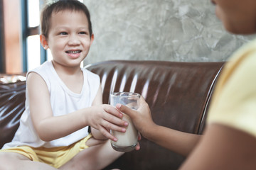 Older sister giving a glass of milk to her young brother to drink in the breakfast time