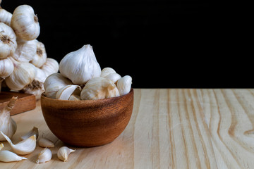 Garlic bulbs in wooden bowl and Garlic cloves on wooden table with copyspace on black background..