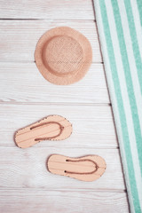 Fototapeta na wymiar Concept of beach holiday. Beach flip-flops, striped cotton towel, grey hat from sun. Summer flat lay with copy space. Summer wooden background. Minimal style.