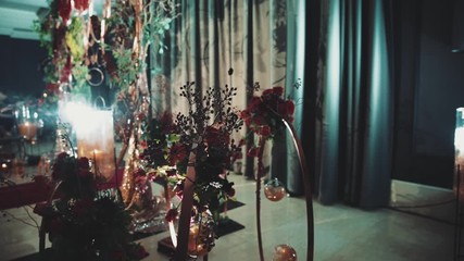 Front view of decorative arch made of greenery and red flowers and leaves for the wedding ceremony, illuminated with metal decorative round structures in the hall