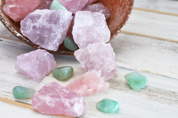 A close up image of a tipped over pottery bowl filled with rose quartz and green aventurine...