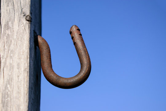 Metal hook in a wooden wall. Background is blue sky. Rusty metal, notches. Profile view.
