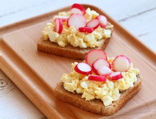 Egg salad over whole grain toast with radish.  Homemade spread made from eggs and processed cheese on the table.