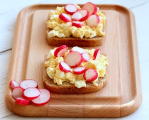 Egg salad over whole grain toast with radish.  Homemade spread made from eggs and processed cheese on the table.