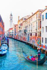 Venetian gondolier punting gondola through green canal waters of Venice Italy