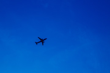 Fototapeta na wymiar The silhouette of an airplane is climbing against a clear blue sky. Place for text or paste, copy place