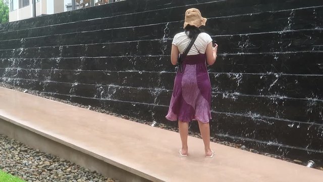 Asian hipster traveler woman with purple dress & sun hat took photo or vdo of water drop from black granite swimming pool at tropical summer resort or hotel, business & travel concept, b-roll footage 