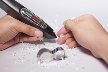 Diamonds in front of a white background, reflections on the ground. brilliant cut diamond held by right hand, diamond testing machine, tester, white gemstone, diamond checking equipment.
