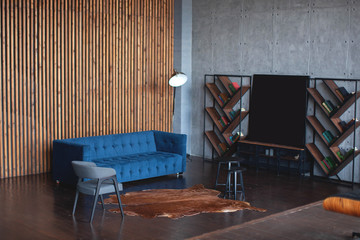 The interior is in a modern style. Dark colors. Blue sofa, lamp, carpet, armchair and bookshelf.