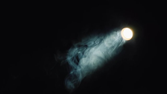 Thin beam of the spotlight illuminates the smoke in the dark