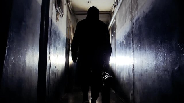 Unrecognizable Man Burglar Wearing Black Jacket and Carrying a Bag Walking Away From the Camera Along Corridor in Old Apartment Building Criminal Concept
