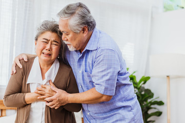 Obraz premium Retired Asian senior elderly wife pain from heart attack disease or illness with serious or worried husband take care at home. Medical emrgency treatment and health care insurance protection concept