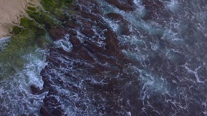 Aerial lock down view: Above the ocean, waves and water surface above coast line