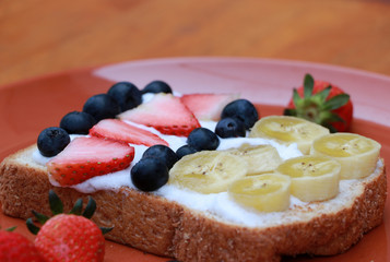 Breakfast in the round plate on the wooden floor. Slice of bread with whipped cream and fruit, Strawberry, Blueberry and Banana.