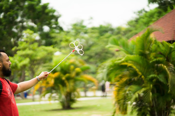 Bearded man playing soap bubbles at the park.