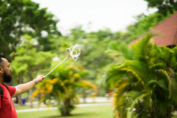 Bearded man playing soap bubbles at the park.