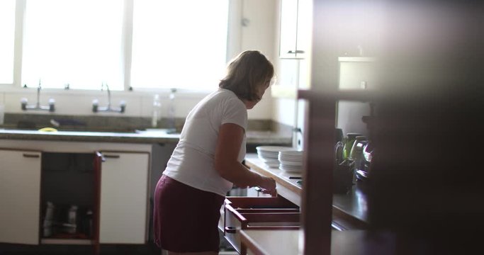 Casual candid older woman cleaning kitchen organizing utensils inside drawers