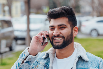 Bearded stylish indian man outdoors using app in his smartphone.