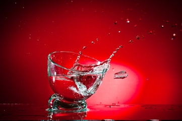 A splash of a drink in a glass, shot against a bright red background.