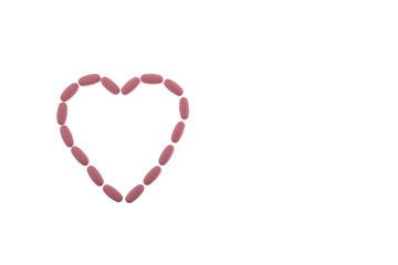 Pink pills in the shape of a heart on a white isolated background. Daily Vitamins dose. Heart shape made of tablets for therapy, concept of treatment and healthcare. Copy space.