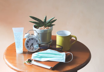 Sansevieria Boncel with alarm clock , yellow cup of coffee , notebook,eye glasses, hygienic mask and alcohol hand gel on wooden table.stay safe, self isolation, quarantine concept.