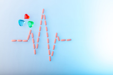 Pills in shape of cardiogram pulse on blue gradient background. Pink vitamins and glass hearts,...