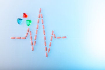 Pills in shape of cardiogram pulse on blue gradient background. Pink vitamins and glass hearts, symbol of healthy lifestyle and copy space. Heartbeat rhythm made of tablets