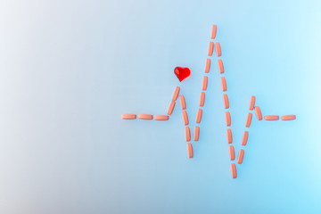 Pills in shape of cardiogram pulse on blue gradient background. Vitamins and red glass heart, symbol of healthy lifestyle. Pharmaceutical and cardiology concept. Heartbeat rhythm made of tablets