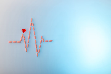 Pills in shape of cardiogram pulse on blue gradient background. Vitamins and red glass heart, symbol of healthy lifestyle. Pharmaceutical and cardiology concept. Heartbeat rhythm made of tablets