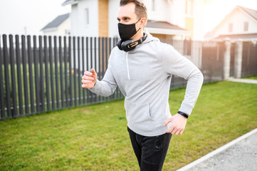 Morning jogging during quarantine. A guy in medicine mask runs and listens music in headphones among country houses