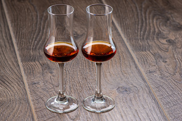 two glasses of sniffer with cognac and waves and splash closeup on wooden background