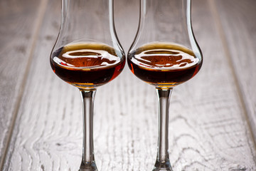 two glasses of sniffer with cognac and waves and splash closeup on wooden background