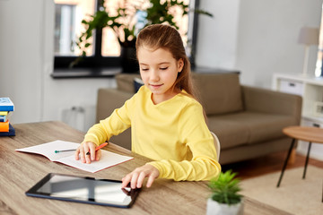 Naklejka premium children, education and school concept - happy student girl with tablet pc computer writing to notebook at home