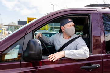 A man in a protective mask driving a car. Portrait of a man in a car in a surgical mask. A man goes to rest in the countryside.