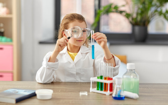 education, science and children concept - girl in goggles with magnifier studying test tube with chemical at home laboratory