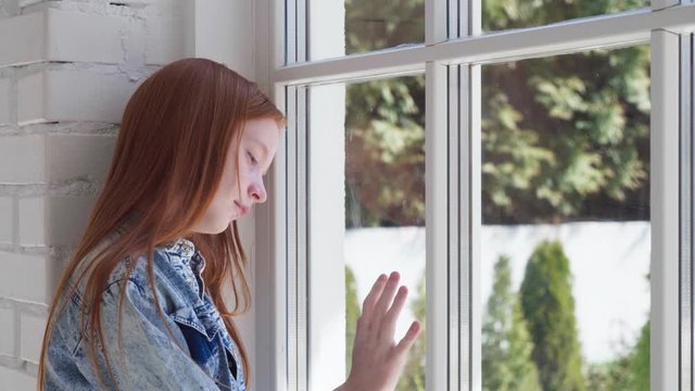Sad teen girl looking out window at home isolation