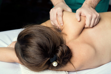 Male hands massage the muscles of the female shoulder blade and shoulder.