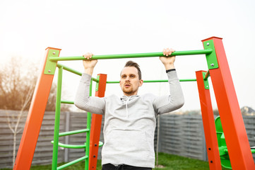 Outdoors workout. An athletic young man is doing pull-ups on the horizontal bar. Healthy lifestyle concept
