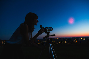 Silhouette of a woman and telescope with twilight sky.