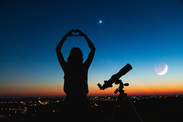 Silhouette of a woman and telescope with twilight sky.