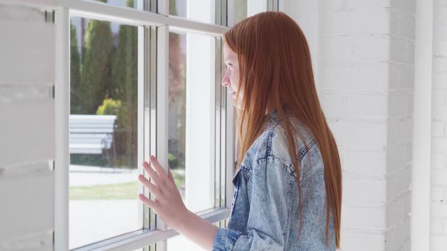 Teenager girl looks out window with curiosity