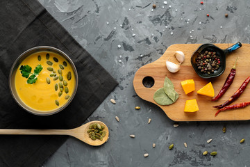 Ready dish of pumpkin soup with ingredients on the wooden board on grey backgound. Top view.  Horizontal