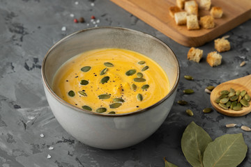 Creamy pumpkin soup with seeds and spices served with crackers on wooden boards on grey backgound. Close up view