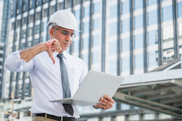 Civil engineering using laptop while working on building construction site and feeling bad with his work.