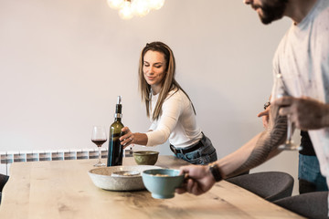 Smiling friends putting snacks and red wine on table. Cheerful young people spending time together....