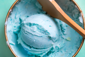 Fresh blue homemade natural ice-cream in a bowl with spoon on a light blue background.