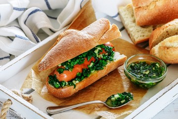 Homemade Delicious baguette sandwich with sausage and Chimichurri Argentinian green sauce made of parsley, garlic, oregano, hot pepper, olive oil, vinegar. Gourmet appetizer. Hotdog. Selective focus