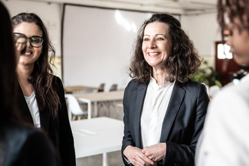 Smiling mature employee with younger colleagues. Cheerful office managers communicating in office. Communication concept