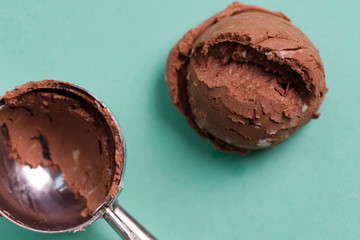 Ball of homemade natural fresh chocolate ice-cream and metallic scoop on a blue background frome the same dessert.