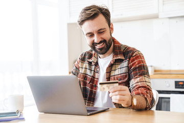 Portrait of cheerful man working with laptop and holding credit card